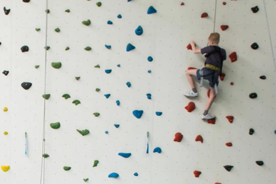 Junge klettert gesichert Kletterwand hoch