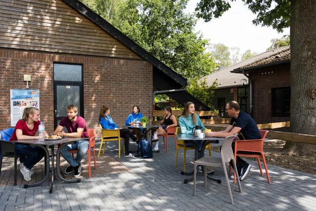Jugendliche und Betreuende sitzen draußen an Tischen mit Getränken