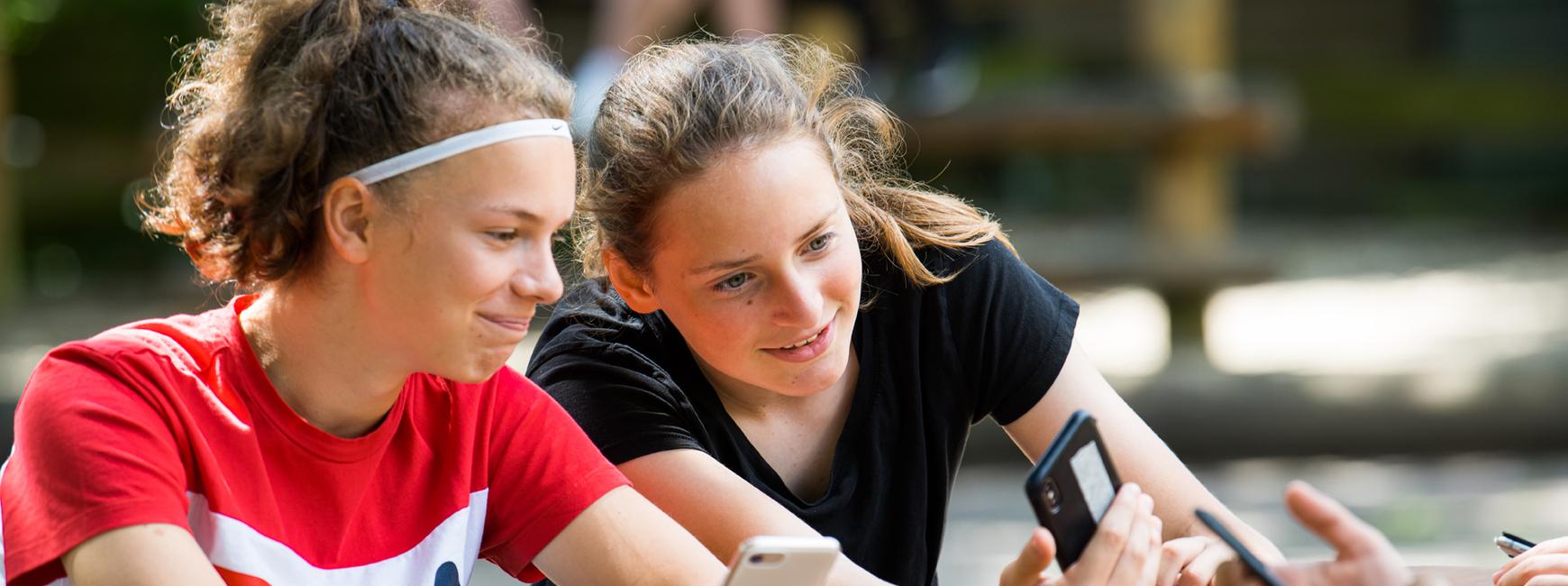 Mädchen sitzen mit Smartphone draußen am Tisch