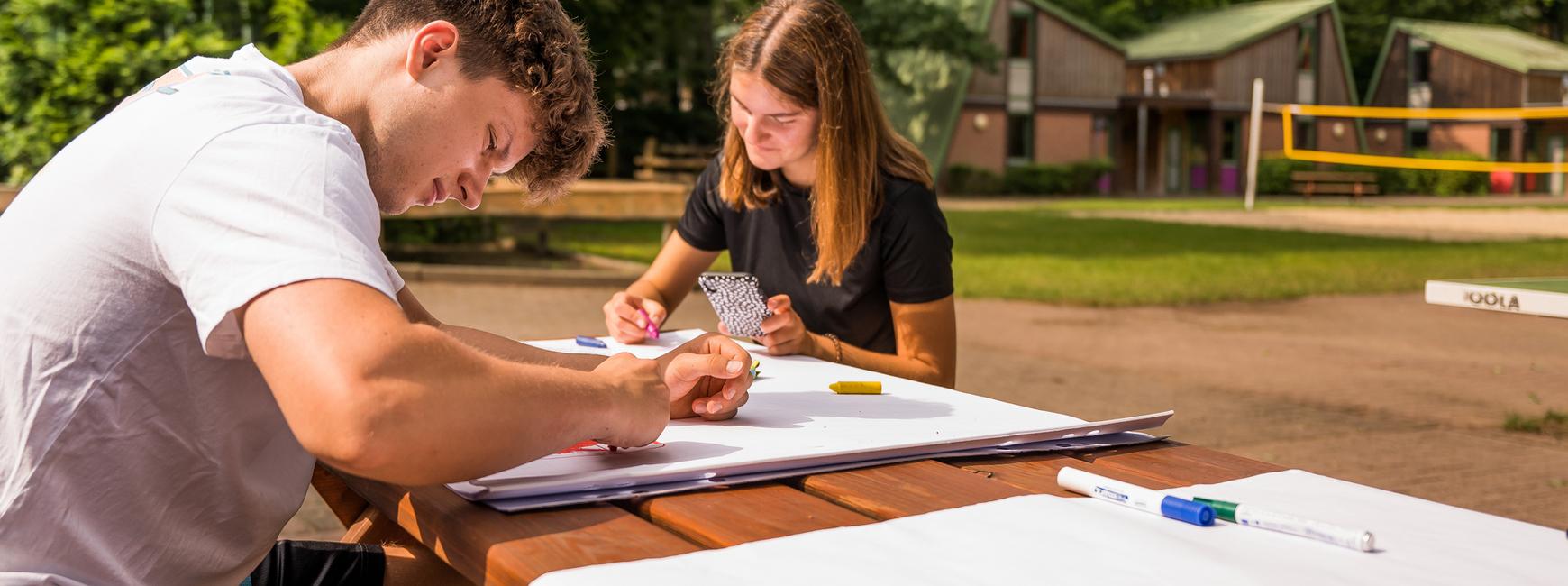 Jugendliche sitzen draußen am Tisch und beschriften Plakate