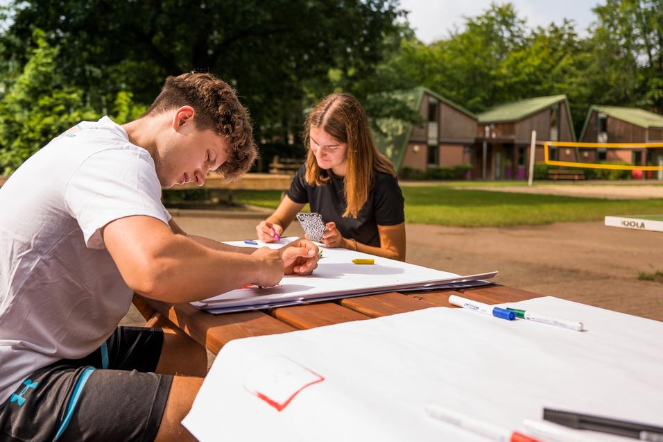 Jugendliche sitzen draußen am Tisch und beschriften Plakate