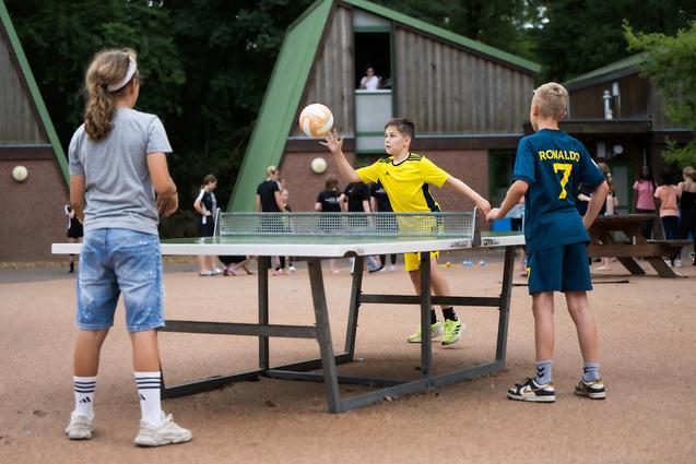 Tischtennisplatte 3 Kinder spielen mit Ball an Tischtennisplatte auf dem Gelände